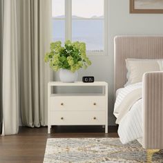 a white bed sitting next to a window covered in curtains and a vase with flowers