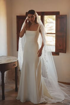 a woman in a wedding dress is standing near a table with a veil on her head