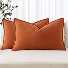 two orange pillows sitting on top of a white couch next to a potted plant