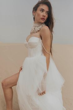 a woman sitting on top of a sand dune wearing a white dress and high heels