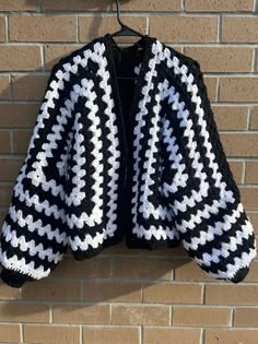 a black and white crocheted jacket hanging on a brick wall