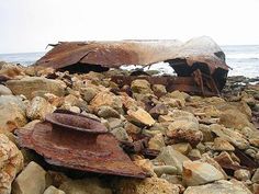 a pile of rocks with a rusted piece of metal on top and water in the background