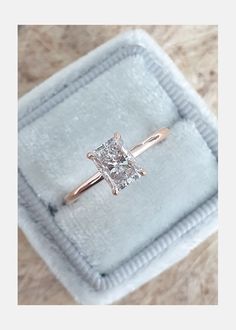 an engagement ring with a princess cut diamond in it on a velvet box that is sitting on the floor