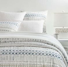 a white bed with blue and green designs on the comforter, pillows and lamps