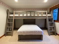 a bunk bed in a room with two ladders on the wall and a white bedspread