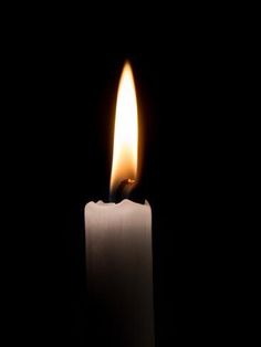 a lit candle in the dark with its light shining on it's side and black background