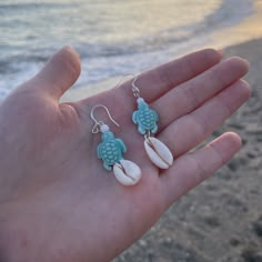 a person is holding some seashells in their hand on the beach near the water