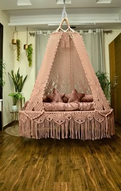 a pink hammock hanging from the ceiling in a room with wood floors and potted plants