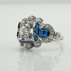 This vintage ring is crafted in solid 14K White Gold (carefully tested and guaranteed). The center Old European cut diamond is .75 carat of VS1 clarity and G color! It is accented with 18 mine cut diamonds of SI1-I1 clarity and H color totaling .38 carat. The blue enamel is in mint condition. The top of the ring measures 13mm top to bottom. The setting elevates 6mm high above finger. Size 4.5 (sizable). The ring weighs 4.2 grams. Great vintage condition. T5183455 Collectible Blue Diamond Cut Ring, Blue Art Deco Diamond Ring Hallmarked, Blue Art Deco Diamond Ring With Hallmark, Blue Art Deco Jewelry Stamped 14k, Classic Hallmarked Enamel Ring For Wedding, Blue Platinum Cluster Ring For Wedding, Blue Platinum Cluster Wedding Ring, Wedding Blue Platinum Cluster Ring, Blue Platinum Jewelry Collectible