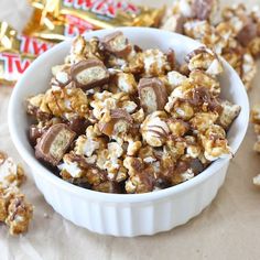 a white bowl filled with caramel popcorn next to two pieces of chocolate and candy bar