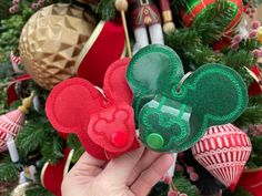 someone is holding two mickey mouse ears in front of a christmas tree with other ornaments