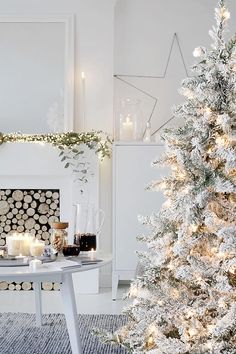 a white christmas tree in front of a fireplace with lit candles and decorations on it