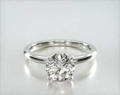 a white gold engagement ring with a round brilliant cut diamond in the center, on a plain surface