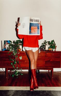 a woman in red sweater and white shorts holding up a magazine