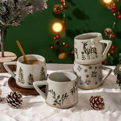 three mugs on a table with pine cones and christmas decorations