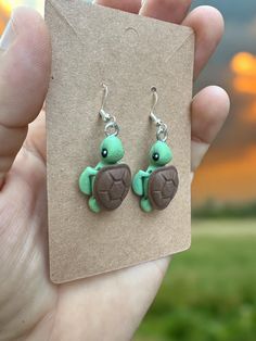 a hand holding a pair of earrings with a turtle on it