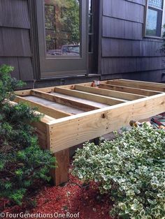 a wooden bed frame sitting in front of a house next to some bushes and trees