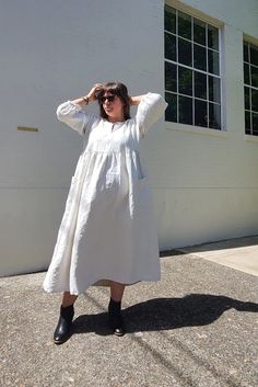 a woman standing in front of a building wearing a white dress and black booties