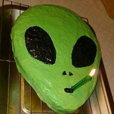 a green cake with a lit candle in it's mouth on a cooling rack