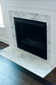 an empty fireplace with white marble surround and wood flooring in a living room area