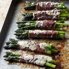 asparagus wrapped in prosciutto and sauce on a baking sheet with parmesan cheese