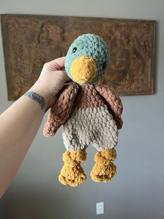 a hand holding a small stuffed animal in front of a wall hanging on the wall