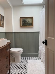 a white toilet sitting in a bathroom next to a wooden dresser and sink under a window