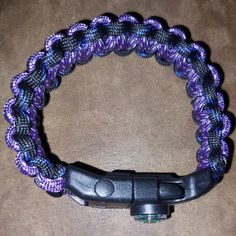 a purple and black braided bracelet on a brown surface with an object in the middle