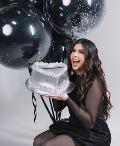 a woman holding a cake and balloons in front of her