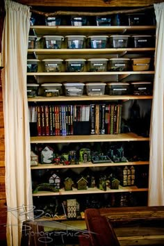 a book shelf filled with lots of books next to a wooden bench and window covered in curtains