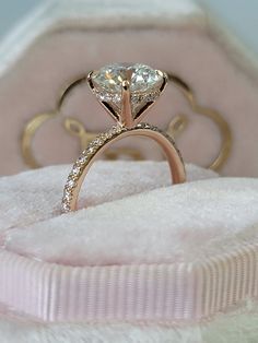 a close up of a diamond ring in a pink velvet box on top of a white blanket