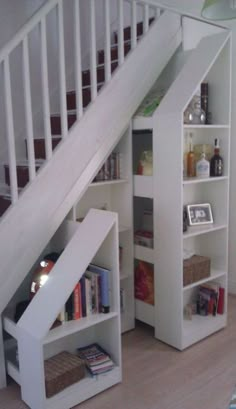 an under the stairs book shelf with books and drinks in it, next to a stair case