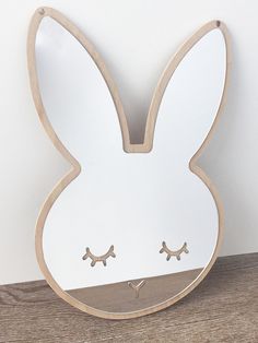 a white wooden bunny shaped clock on a wood shelf with two eyes and one nose