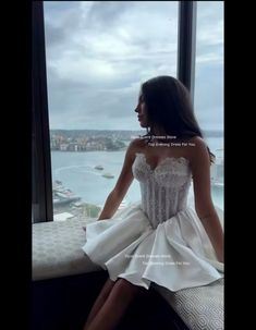 a woman sitting on top of a window sill looking out at the water and buildings