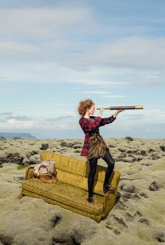 a woman sitting on top of a couch with a telescope in her hand and looking into the distance