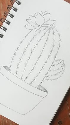 a drawing of a cactus in a pot on a wooden table next to a pen and paper