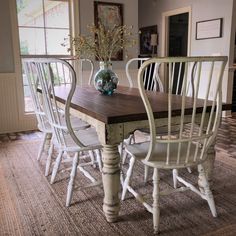 a dining room table with four chairs and a vase on top of it in front of a window