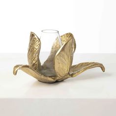 a gold flower shaped vase sitting on top of a white tableclothed surface with a wine glass in the middle