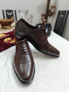 A chocolate brown classic Oxford shoe is a timeless and versatile footwear choice for both formal and semi-formal occasions.  It follows the classic Oxford shoe style, characterised by its closed lacing system, which gives it a sleek and formal appearance. The shoe has a plain, unadorned design, emphasizing its elegance. The upper of the shoe is made of high-quality, supple leather with a polished finish. This not only enhances the shoe's aesthetics but also adds to its durability and longevity. Classic Brown Closed Toe Lace-up Shoes, Brown Lace-up Derby Shoes For Business, Brown Closed Toe Business Leather Shoes, Brown Closed Toe Business Oxfords, Brown Business Oxfords, Brown Fitted Closed Toe Dress Shoes, Fitted Brown Closed Toe Dress Shoes, Classic Brown Almond Toe Oxfords, Fitted Brown Closed-toe Dress Shoes