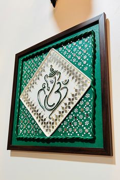 an intricately designed wall hanging on the side of a white wall with green and brown trim