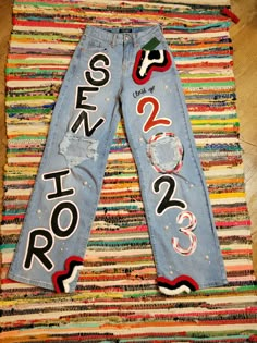 a pair of jeans that have been decorated with letters and numbers on the side, sitting on top of a multicolored rug