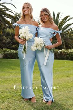 two beautiful women standing next to each other in blue dresses holding bouquets of flowers