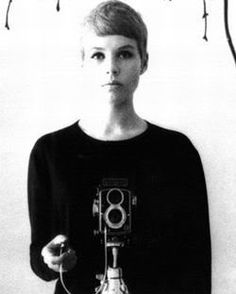 black and white photograph of a woman holding an old camera in front of her face