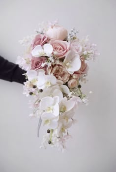 a bridal bouquet with pink roses and white orchids is being held by someone's hand