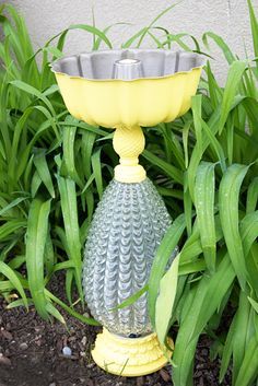 a yellow vase sitting on top of a flower pot next to some green plants and grass