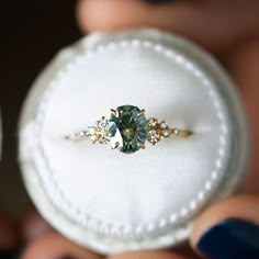 a ring with a green stone in it being held up by someone's hands