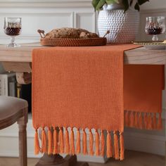 an orange table runner with tassels sits on top of a dining room table