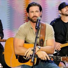 two men are playing guitars and singing into microphones in front of a colorful background