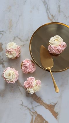 cupcakes with pink and white frosting sitting on a plate next to a spoon