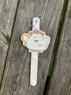 a keychain with an elephant on it hanging from a wooden fence, next to a piece of wood